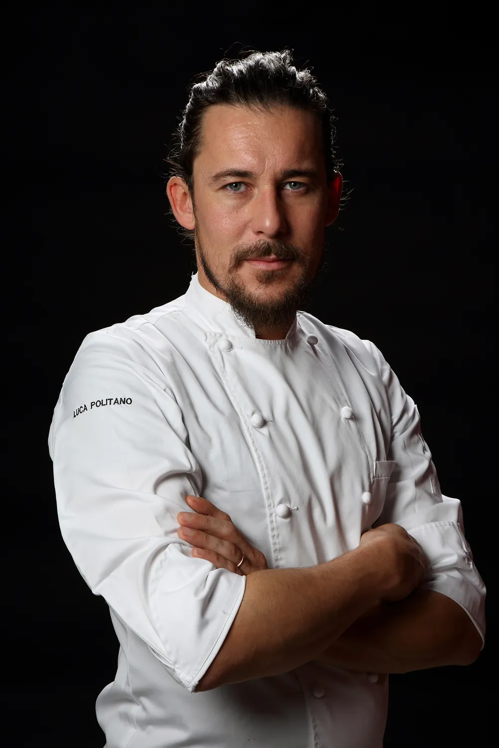 Portret van chef Luca Politano in wit koksbuis tegen een zwarte achtergrond